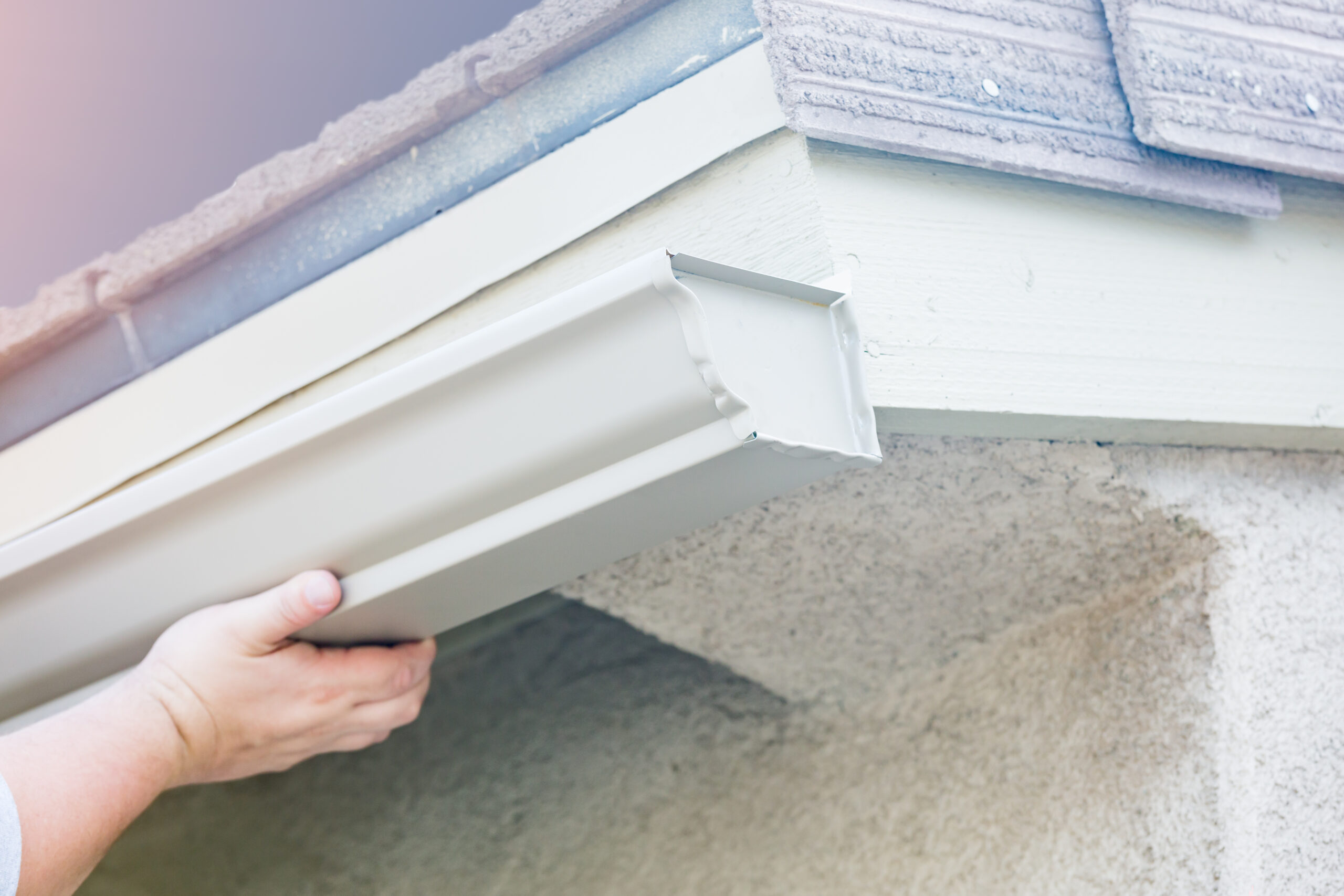 Worker attaching aluminum rain gutter to fascia of house.