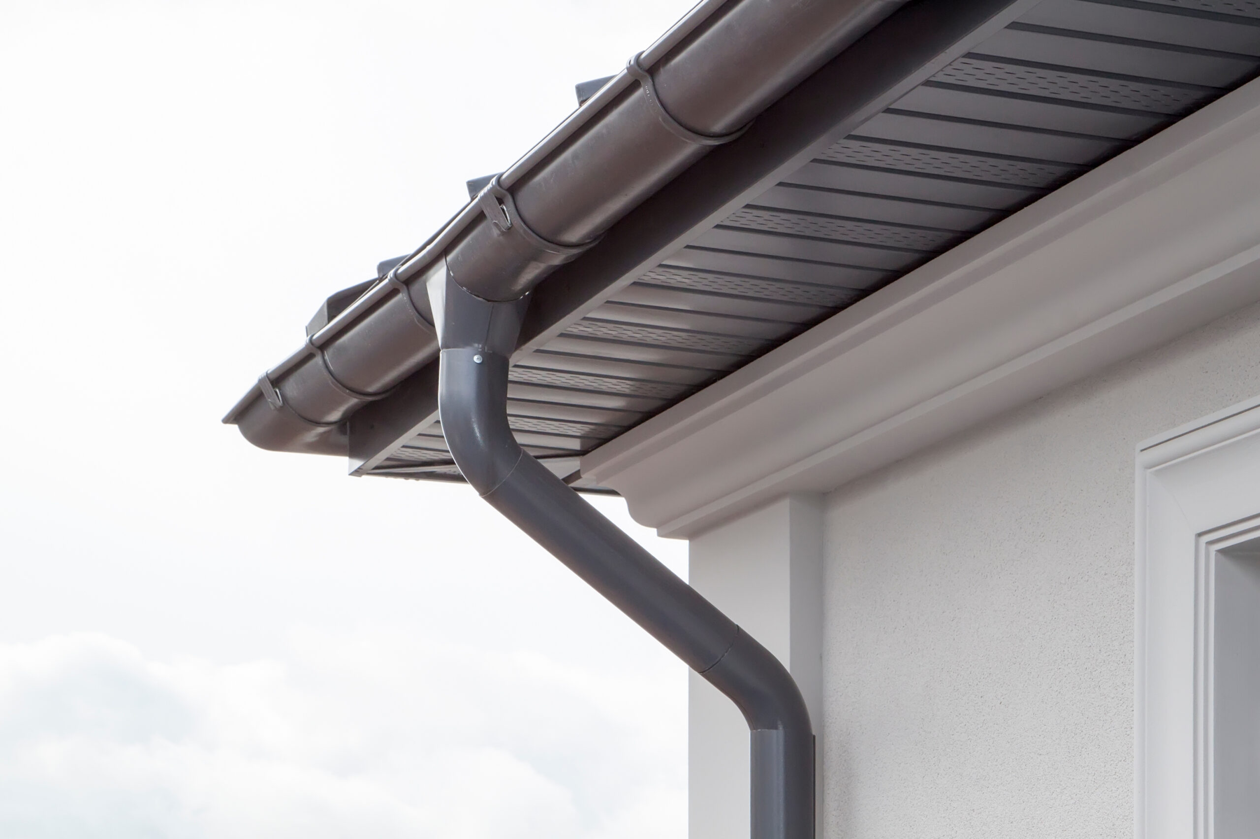 Corner of the house with new gray metal tile roof and rain gutter. metallic guttering system, guttering & drainage pipe exterior